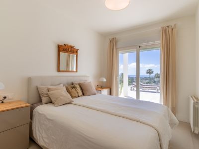 Chambre lumineuse avec lit, tables de chevet et accès direct à une terrasse offrant une vue panoramique sur la mer et des chaises longues.