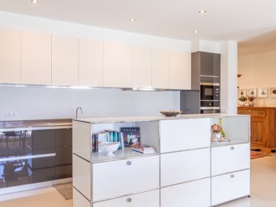 Cuisine moderne avec meubles hauts laqués beige clair et bas gris foncé. Îlot central intégrant rangements ouverts et électroménagers encastrés.