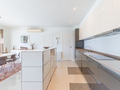 Cuisine moderne ouverte avec des armoires laquées blanches et gris foncé, une plaque à induction intégrée et un îlot modulaire. Coin repas adjacent avec table ovale et chaises en bois.