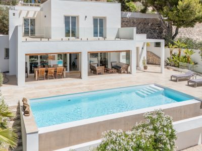 Extérieur de villa moderne avec piscine rectangulaire à marches et vaste terrasse en pierre claire. Comprend un coin repas extérieur, un salon et un balcon supérieur avec garde-corps en verre.
