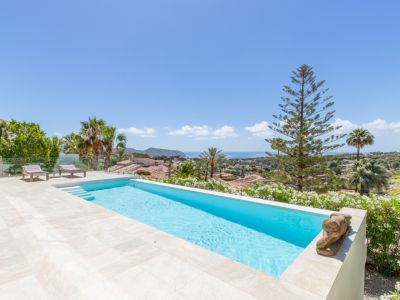 Piscine à débordement carrelée de bleu clair, terrasse en grès beige et vue panoramique sur la mer Méditerranée. Deux chaises longues et une végétation méditerranéenne luxuriante.