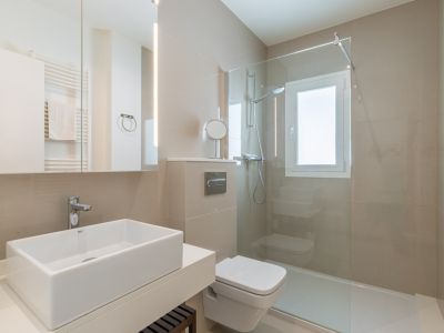 Salle de bain contemporaine avec lavabo rectangulaire, WC suspendu et douche à l'italienne vitrée. Carrelage neutre et miroir éclairé par LED verticale définissent l'espace.