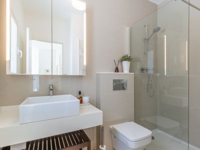 Salle de bain moderne avec lavabo rectangulaire sur meuble suspendu, miroir éclairé par LED et douche vitrée. Revêtement mural en carreaux neutres.