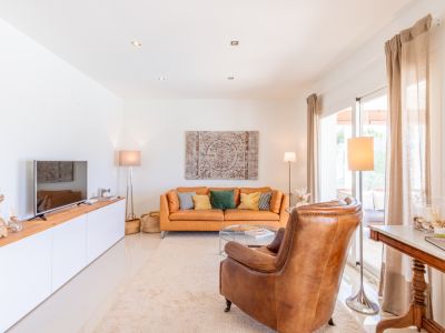 Salon lumineux avec un canapé en cuir couleur terre de Sienne, un fauteuil et un meuble TV. Des portes coulissantes vitrées mènent à l'extérieur.