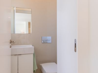 Toilettes modernes avec lavabo rectangulaire et meuble sous-vasque blanc, miroir mural et WC suspendu. Les murs sont recouverts de carrelage beige clair.