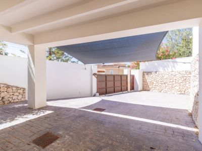 Vaste carport privé avec pavé texturé, voile d'ombrage protecteur et portail coulissant métallique sécurisé, encadré de murs blancs et en pierre naturelle.