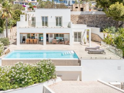 Villa moderne à deux étages avec piscine rectangulaire et grande terrasse carrelée. Comprend un espace repas extérieur couvert et une balustrade en verre, intégrant le design au paysage méditerranéen.