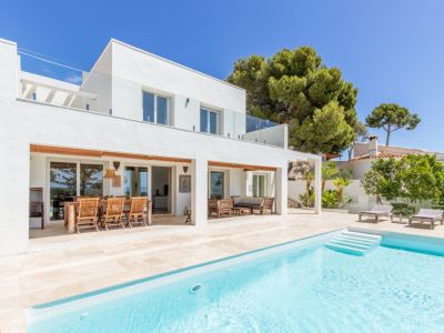 Villa moderne avec piscine carrelée claire et vastes terrasses. Elle dispose d'un coin repas extérieur couvert, d'un espace salon et de balustrades en verre à l'étage.