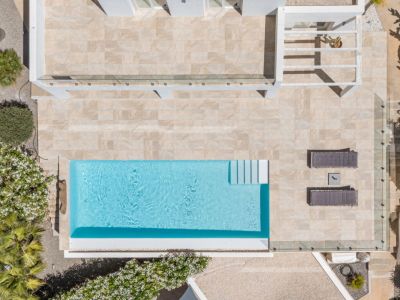 Vue aérienne de la piscine rectangulaire bleue, entourée d'une vaste terrasse carrelée claire, avec transats et végétation méditerranéenne.