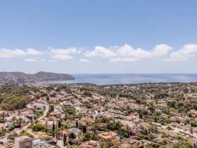 Vue aérienne panoramique d'une zone résidentielle côtière, avec des toits en terre cuite, une végétation luxuriante et la mer Méditerranée à l'horizon.