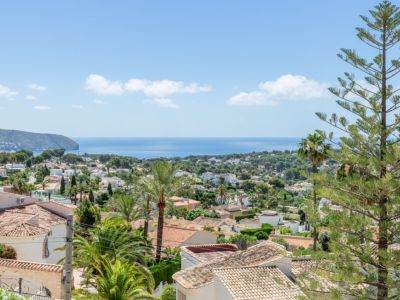 Vue côtière élevée présentant des toits en tuiles, une végétation méditerranéenne luxuriante et un cap rocheux s'avançant dans la mer bleue sous un ciel clair.