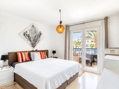 Chambre principale lumineuse avec accès direct à une terrasse privée, sol en marbre et vue sur les palmiers. Une lampe suspendue distinctive et de l'art abstrait complètent l'espace.