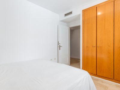 Chambre secondaire avec grand placard intégré en bois clair et lit habillé de linge blanc. Le sol présente un carrelage effet marbre et une porte ouverte mène à une autre pièce.