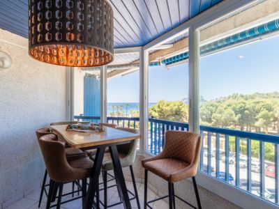 Espace repas vitré avec table haute en bois, tabourets rembourrés et suspension noire. Vues panoramiques sur mer, plage et pinède par les grandes fenêtres.