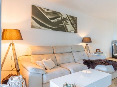Salon avec canapé sectionnel clair, table basse blanche et deux lampadaires trépied en bois. Une grande œuvre d'art représentant un piano décore le mur.
