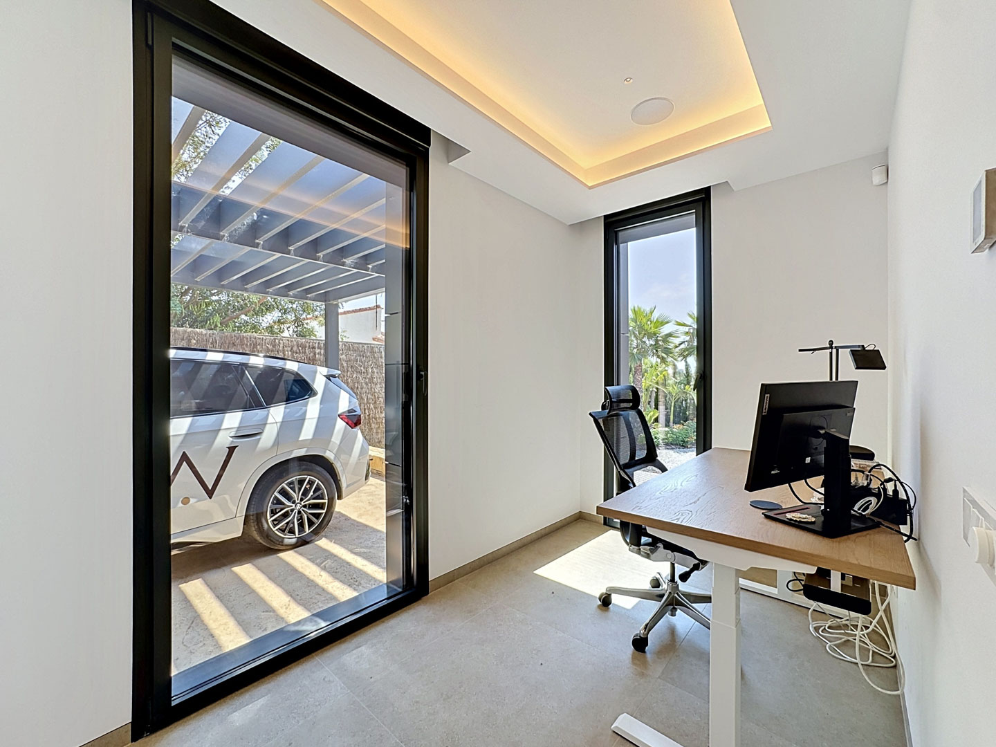 Bureau à domicile contemporain avec bureau en chêne clair, chaise ergonomique et lumière naturelle abondante d'une porte coulissante donnant sur un carport et une fenêtre sur le jardin tropical.