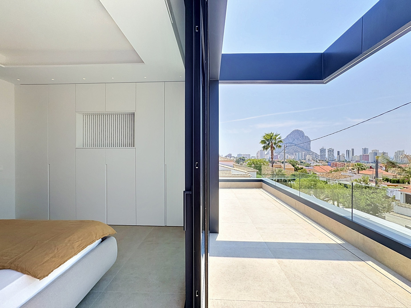 Chambre moderne avec placards intégrés blancs et accès direct à une terrasse spacieuse. Vues panoramiques sur Calpe et le majestueux Peñón de Ifach.