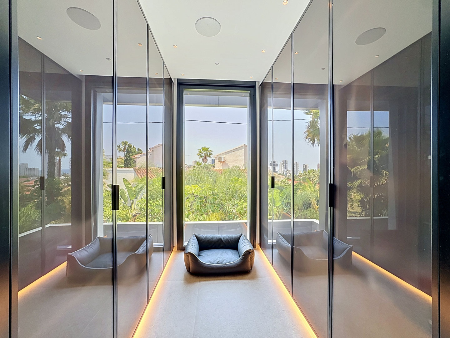 Dressing épuré avec placards miroirs toute hauteur, éclairage de sol intégré et grande fenêtre offrant une vue sur la verdure tropicale.