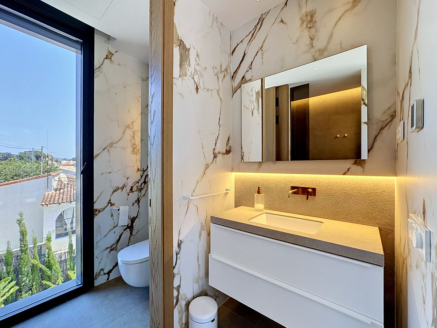 Salle de bain design avec carrelage mural effet marbre veiné et grande fenêtre offrant des vues résidentielles. Comprend une vanité flottante avec plan de travail texturé et robinetterie murale.