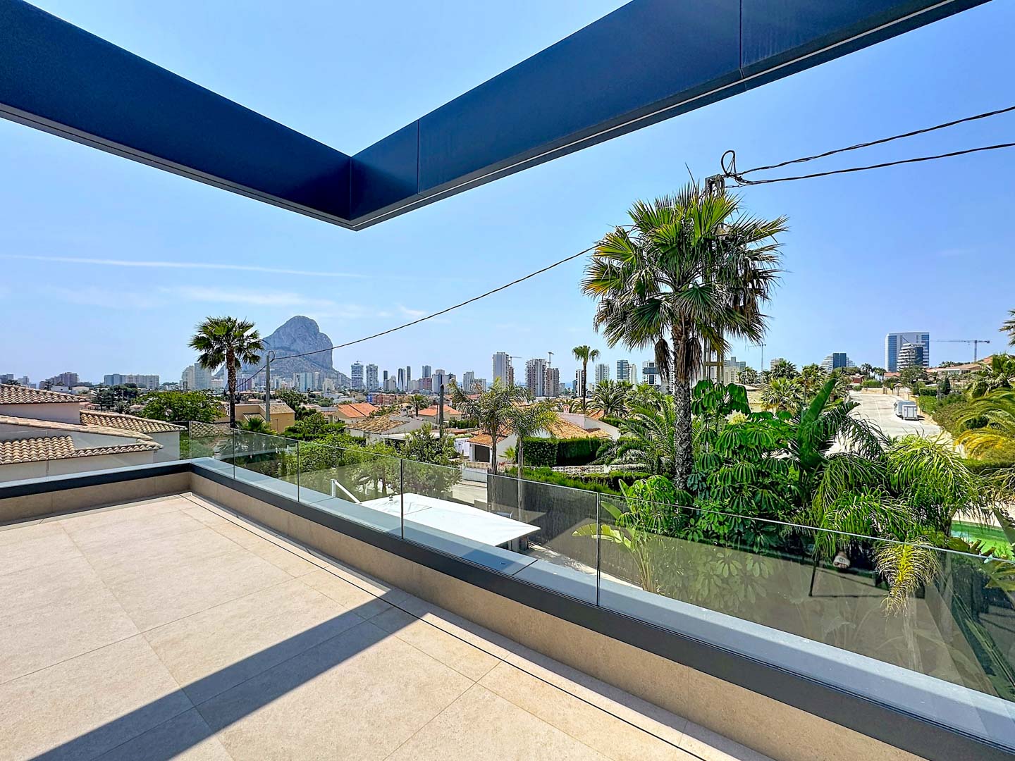 Terrasse supérieure avec carrelage clair et balustrade en verre, offrant des vues panoramiques sur Calpe, le Peñón de Ifach et la ville.