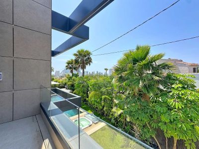 Balcon moderne avec façade à panneaux gris et garde-corps en verre, dévoilant des jacuzzis extérieurs, une végétation tropicale luxuriante et la skyline de Calpe.