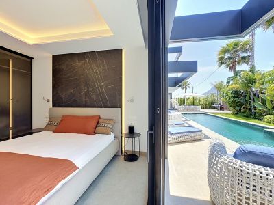 Chambre à coucher avec accès direct à la piscine privée et au jardin tropical luxuriant. Présente un mur d'accent en marbre foncé avec éclairage intégré et des chaises longues modernes.
