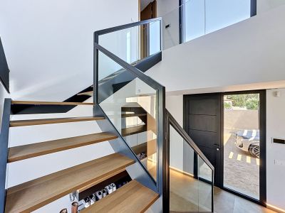Escalier flottant contemporain avec marches en chêne clair et balustrade en verre, éclairé naturellement dans un hall d'entrée à double hauteur.