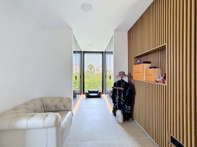 Espace dressing raffiné avec mur à lattes de bois et étagère intégrée, un canapé en cuir capitonné et de larges portes vitrées donnant sur la verdure extérieure.
