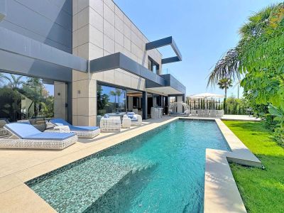 Extérieur de villa contemporaine avec piscine privée en mosaïque, entourée d'une terrasse carrelée claire et de mobilier de salon en rotin blanc. Jardins tropicaux luxuriants et pelouse soignée complètent l'oasis.