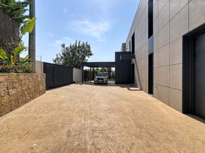 Large entrée avec pavé en béton texturé, mur en pierre naturelle et portail automatique sombre. Façade moderne à panneaux gris et carport intégré.