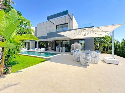 L'extérieur de la villa révèle une piscine rectangulaire, une terrasse carrelée claire avec mobilier de salon blanc moderne et un grand parasol déporté, complété par un aménagement paysager tropical.
