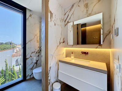 Salle de bain design avec carrelage mural effet marbre veiné et grande fenêtre offrant des vues résidentielles. Comprend une vanité flottante avec plan de travail texturé et robinetterie murale.