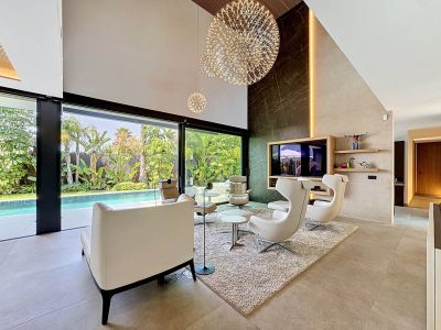 Salon contemporain à double hauteur avec mur d'accent effet marbre foncé, lustres sphériques et grandes portes vitrées donnant sur une piscine privée et un jardin tropical luxuriant.