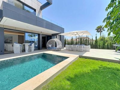 Terrasse extérieure avec piscine en mosaïque bleue, pelouse et mobilier de designer blanc. La façade moderne de la villa s'ouvre sur cet espace de détente avec coin repas ombragé et barbecue.