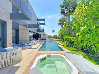 Terrasse extérieure avec piscine rectangulaire et jacuzzi intégré. Le mobilier de salon blanc et bleu s'harmonise avec la façade moderne de la villa et le jardin tropical luxuriant.