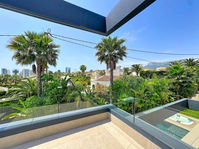 Terrasse supérieure avec sol carrelé et balustrade en verre, offrant des vues sur la végétation luxuriante, la ville et les montagnes, avec la piscine et le jacuzzi intégrés en contrebas.