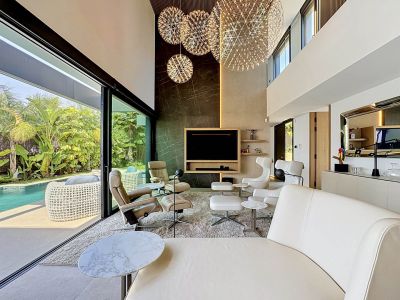 Vaste salon double hauteur avec de grandes baies vitrées donnant sur la piscine privée et le jardin luxuriant. Il présente trois lustres sphériques et un revêtement mural en marbre.
