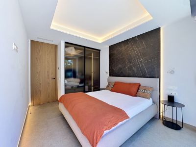 Vaste salon double hauteur avec habillage en bois de chêne, cheminée moderne intégrée et grandes baies vitrées donnant sur des jardins luxuriants. La lumière naturelle inonde cet espace minimaliste.
