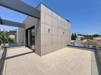 Vaste terrasse supérieure avec carrelage clair et garde-corps en verre, sous des poutres structurelles. La façade moderne à panneaux offre des vues résidentielles.