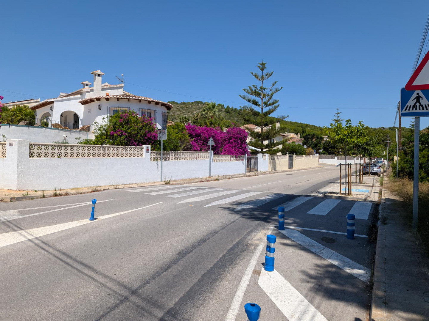 Rue résidentielle avec passage piéton, villa blanche traditionnelle et bougainvilliers éclatants sous un ciel bleu clair. Rue résidentielle avec passage piéton, villa blanche traditionnelle et bougainvilliers éclatants sous un ciel bleu clair.