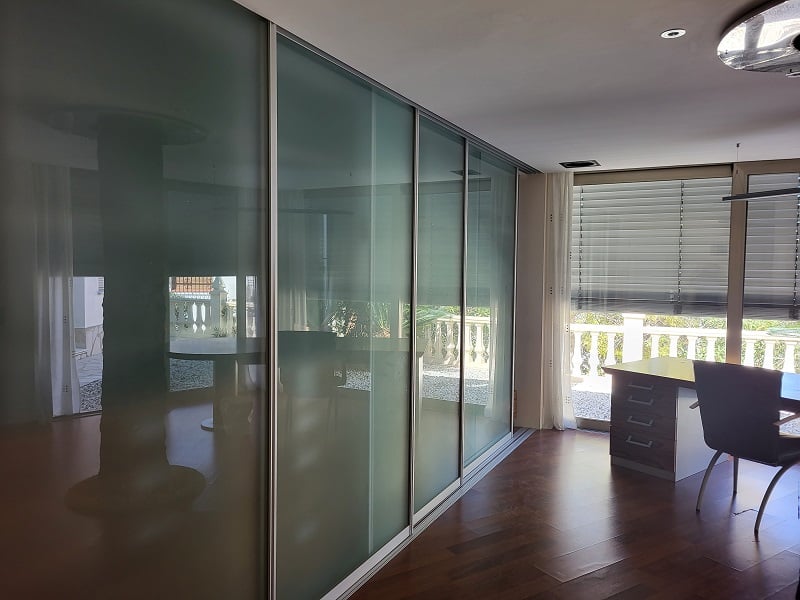 Bureau ou chambre avec d'élégantes portes coulissantes en verre dépoli, parquet en bois foncé et espace de travail près de la fenêtre avec vue sur la balustrade.