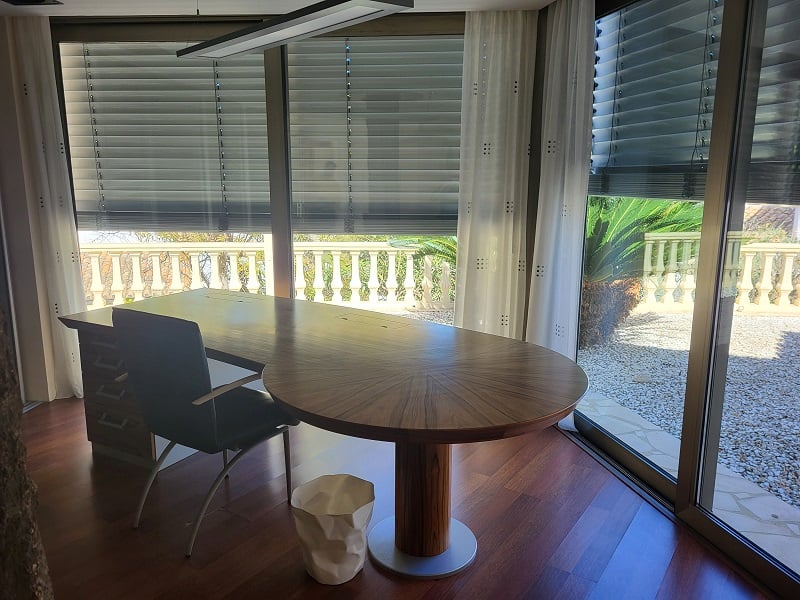 Bureau privé spacieux avec un grand bureau en bois et parquet. Les baies vitrées donnent sur une balustrade et un jardin méditerranéen.