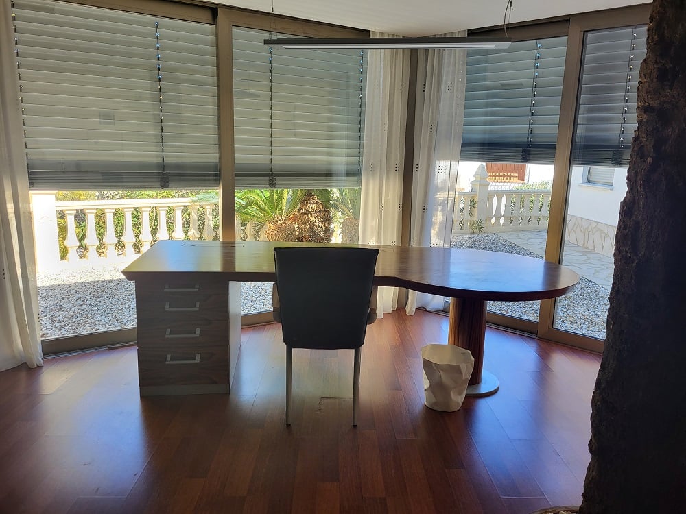 Bureau privé spacieux avec un grand bureau en bois sur mesure et de larges baies vitrées donnant sur un patio gravillonné et un jardin méditerranéen. Parquet foncé et éclairage moderne.