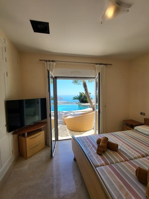Chambre lumineuse avec lits jumeaux et télévision, s'ouvrant directement sur une terrasse. Profitez des vues imprenables sur la piscine à débordement et la mer Méditerranée.