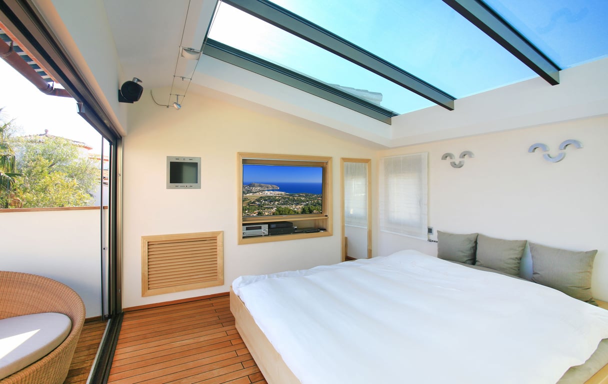 Chambre lumineuse avec un grand puits de lumière en verre et un parquet chaleureux. Une porte coulissante mène à une terrasse privée et une télévision intégrée.