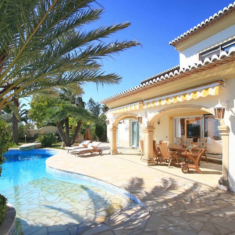 L'extérieur de la villa comprend une piscine de forme libre et une vaste terrasse dallée en pierre menant à une naya couverte avec un ensemble de salle à manger en bois sous des auvents rayés.