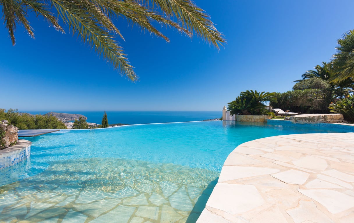 Piscine à débordement avec une entrée en pente douce et margelles en pierre claire, offrant une vue imprenable sur la mer Méditerranée.
