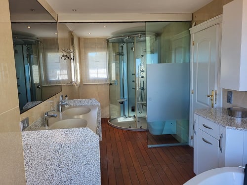 Salle de bain principale avec double vasque au design unique sur base de galets, douche hydromassante vitrée et sol en bois. Grande glace et lumière naturelle.