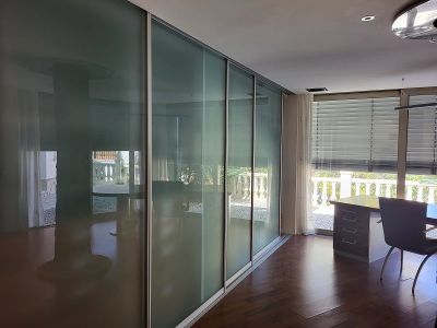 Bureau ou chambre avec d'élégantes portes coulissantes en verre dépoli, parquet en bois foncé et espace de travail près de la fenêtre avec vue sur la balustrade.