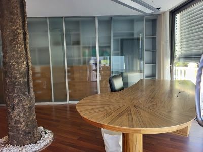 Bureau privé spacieux avec un bureau en bois au design unique, des portes coulissantes en verre dépoli, un arbre intérieur et une luminosité naturelle abondante.